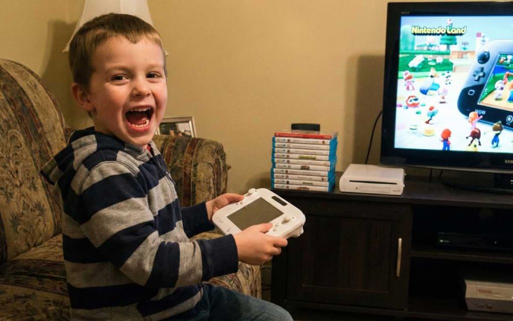 Excited young boy holding a white Wii U GamePad controller in front of a TV, representing the fun of the 2012 console launch